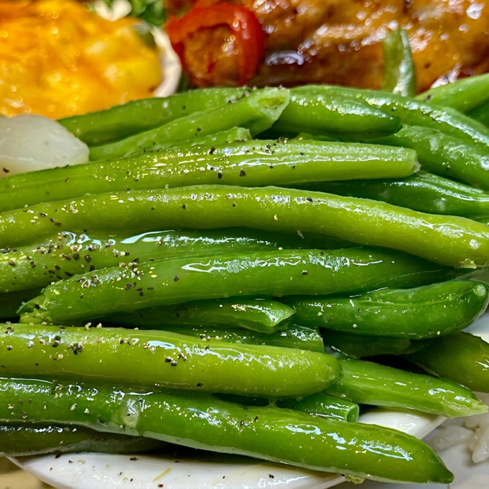 Plate of glossy green beans with rice, roasted vegetables, and a golden cornbread-like side dish.