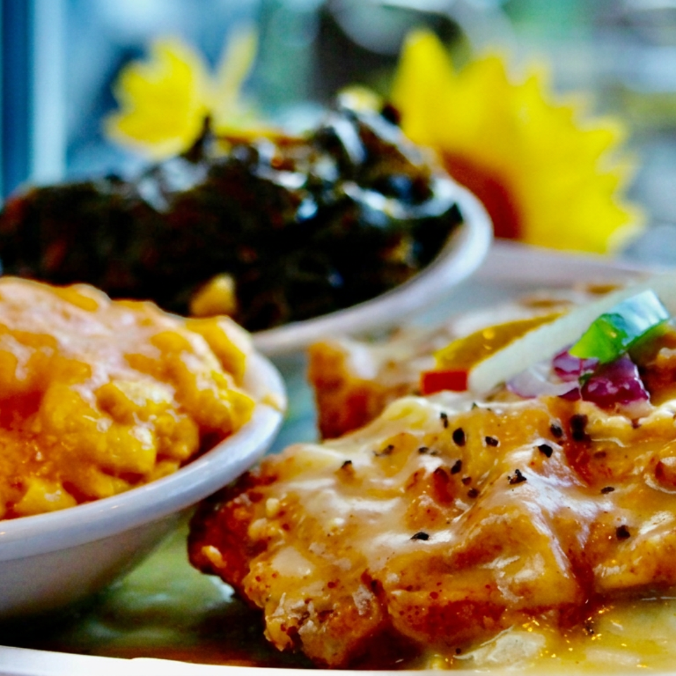 Close-up of saucy golden chicken with rice and vegetables, accompanied by a bowl of curry and dark beans on a restaurant table.