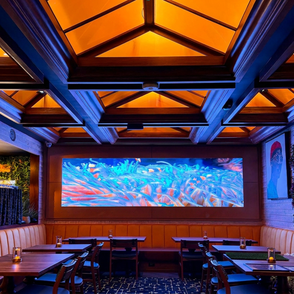 Elegant restaurant dining room with amber backlit ceiling, leather booths, set tables, artwork, and a colorful abstract wall display.