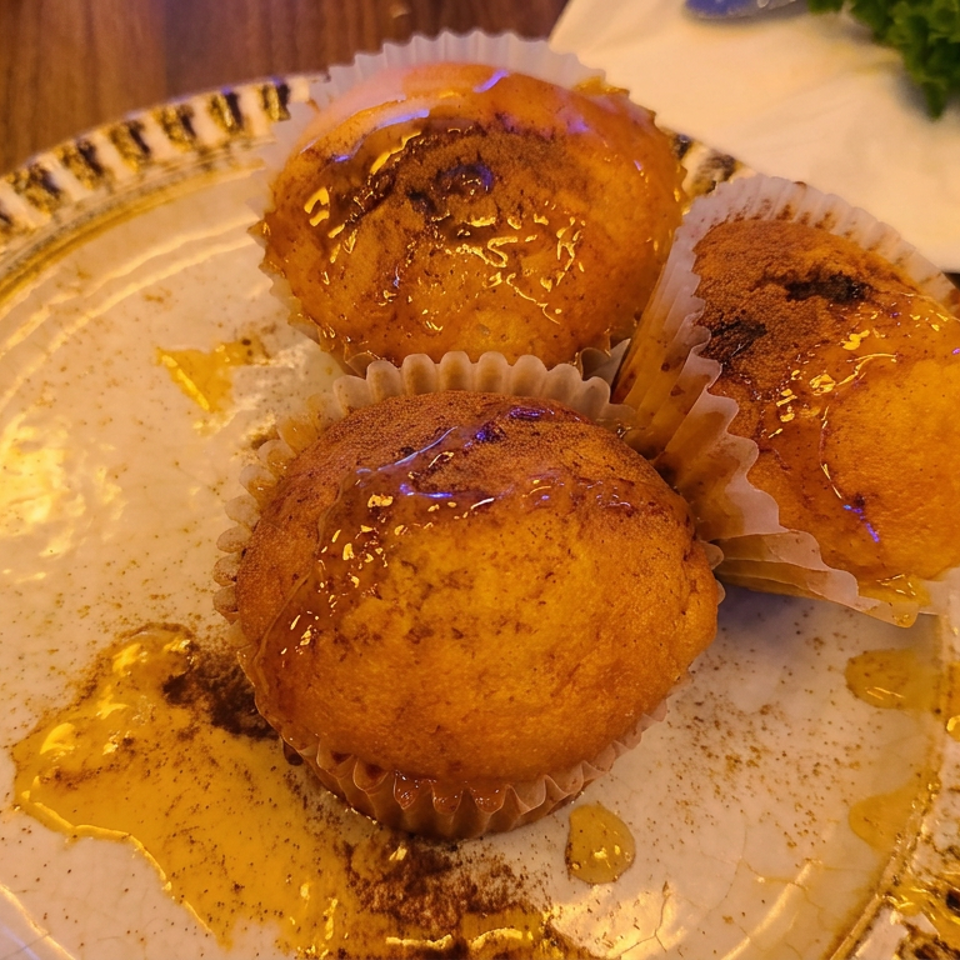 Three golden glazed pastries sit in paper cups on a decorative plate beside a folded napkin and parsley.