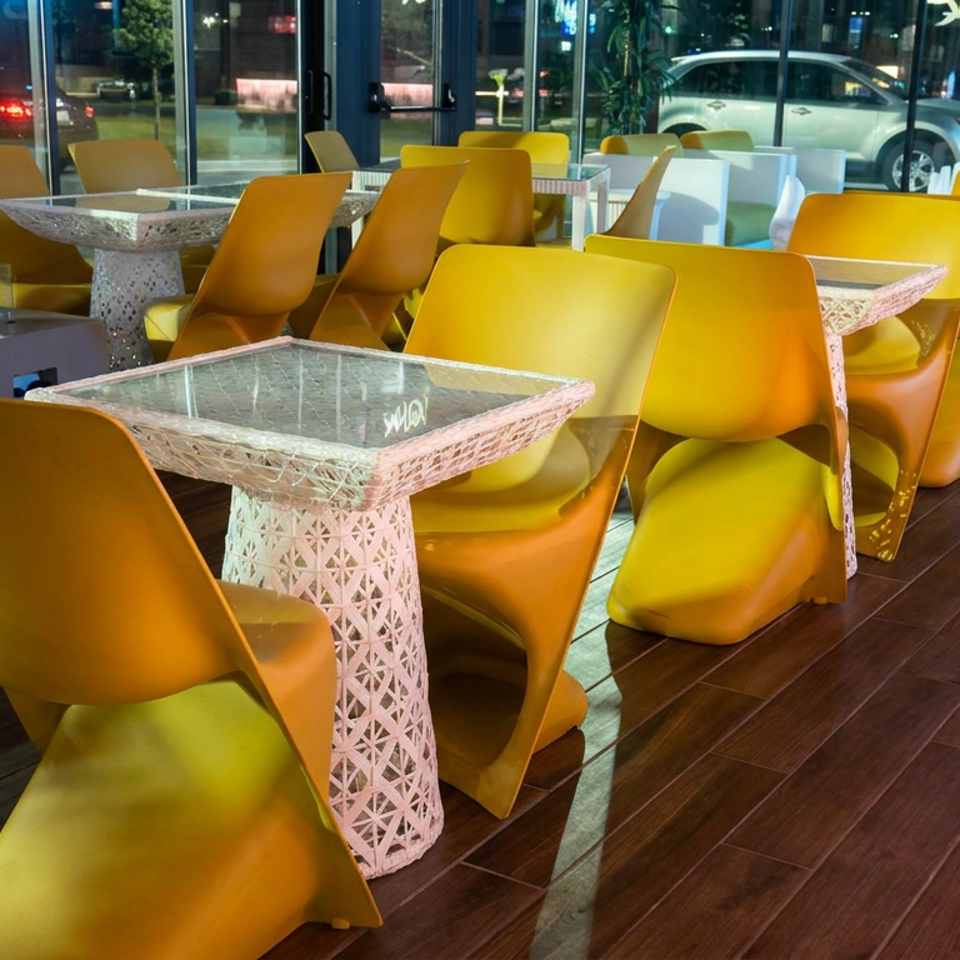 Modern restaurant dining area with bright yellow chairs, decorative mosaic tables, dark wood floors, and floor-to-ceiling windows overlooking the street.