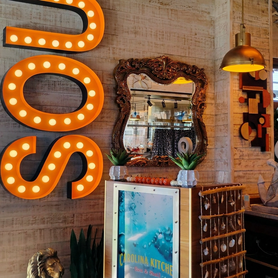 Eclectic Carolina Kitchen restaurant interior featuring illuminated orange wall letters, an ornate mirror, nautical decor, and plants.