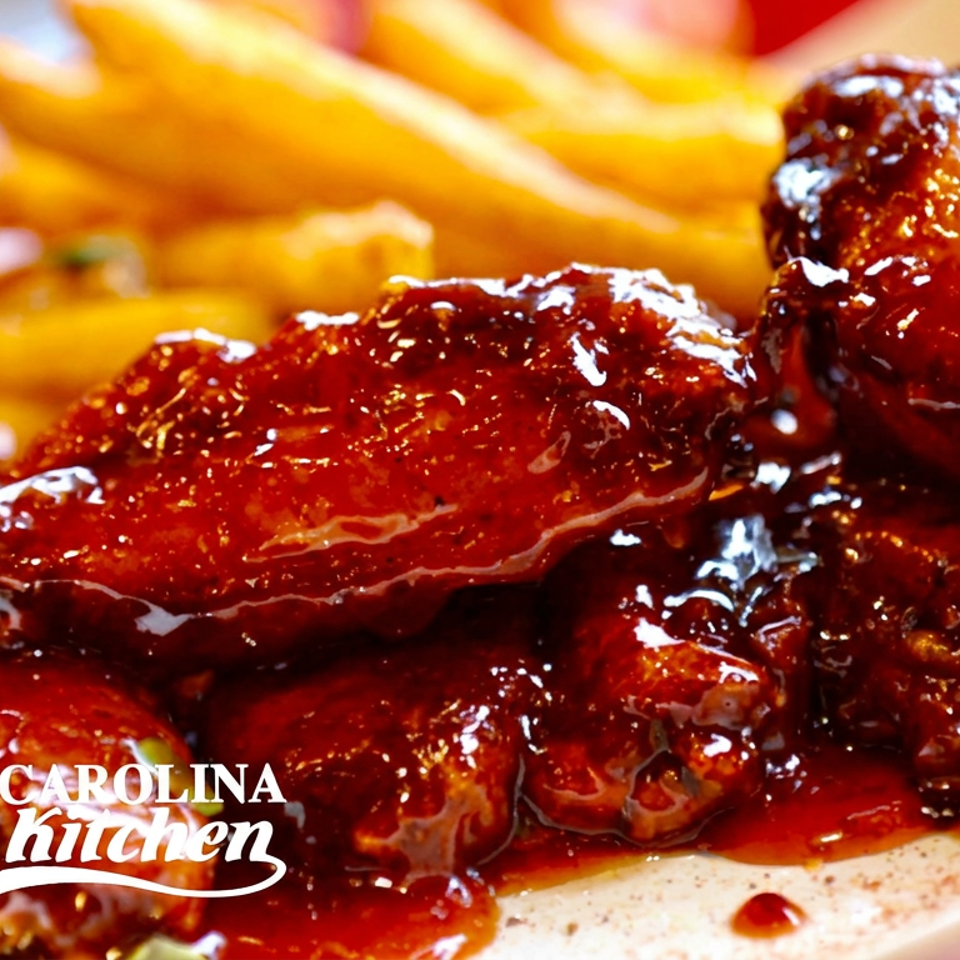 Glossy barbecue chicken wings served with golden fries on a plate, branded Carolina Kitchen.